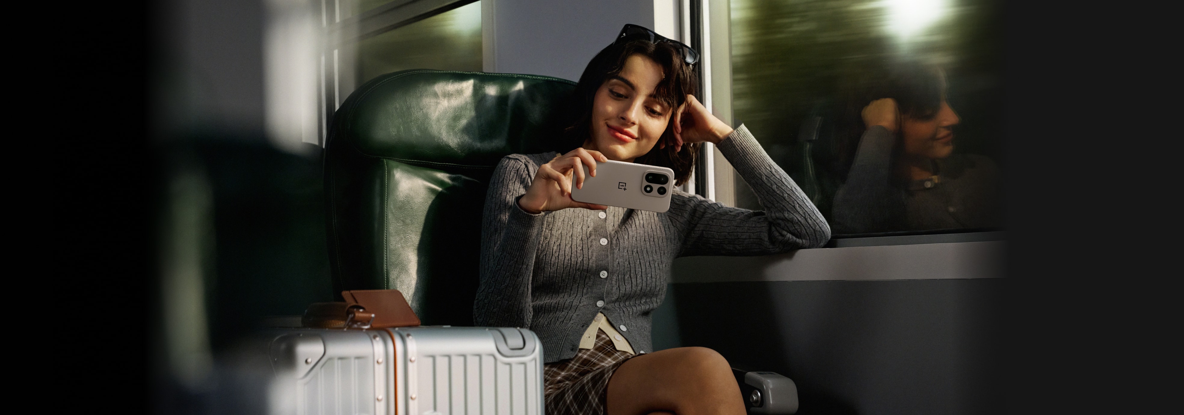 A woman in a gray sweater takes a photo with her smartphone while seated on a train.