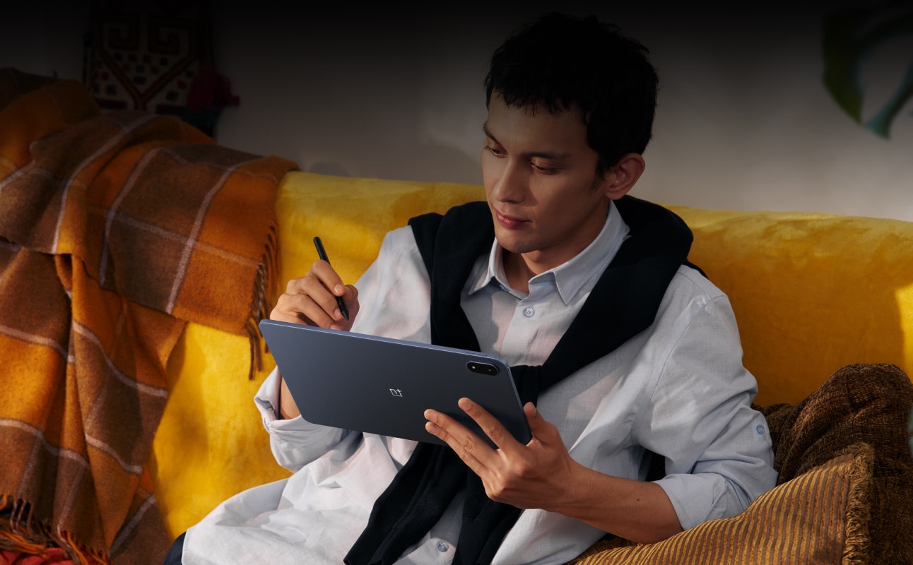 Young man in white shirt working on digital tablet on yellow couch.