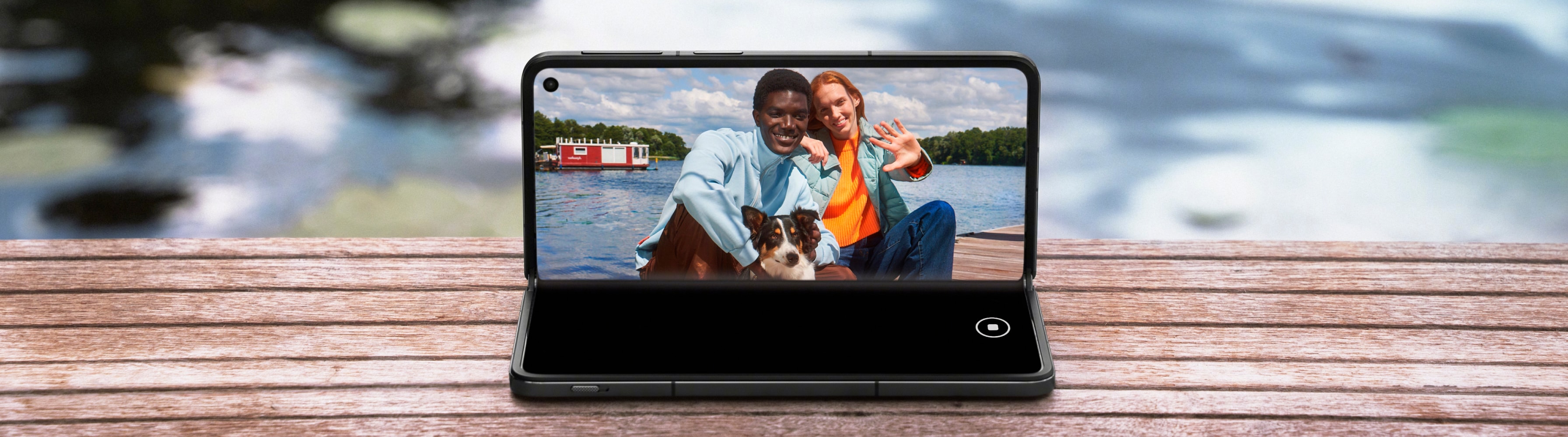 A happy couple sitting on a dock with their dog, enjoying the scenic lake view displayed on a smartphone screen.